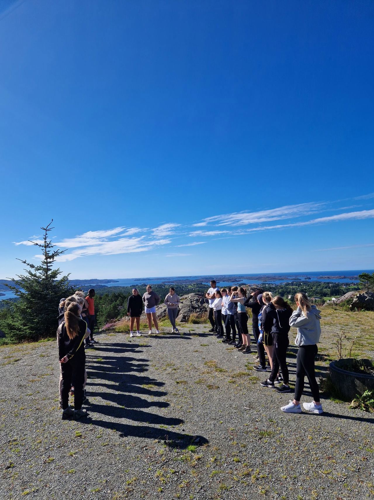 Elevar står på to rekker på in grusplass. Mellom dei står tre elevar. Det ser ut som om dei leikar ein leik.