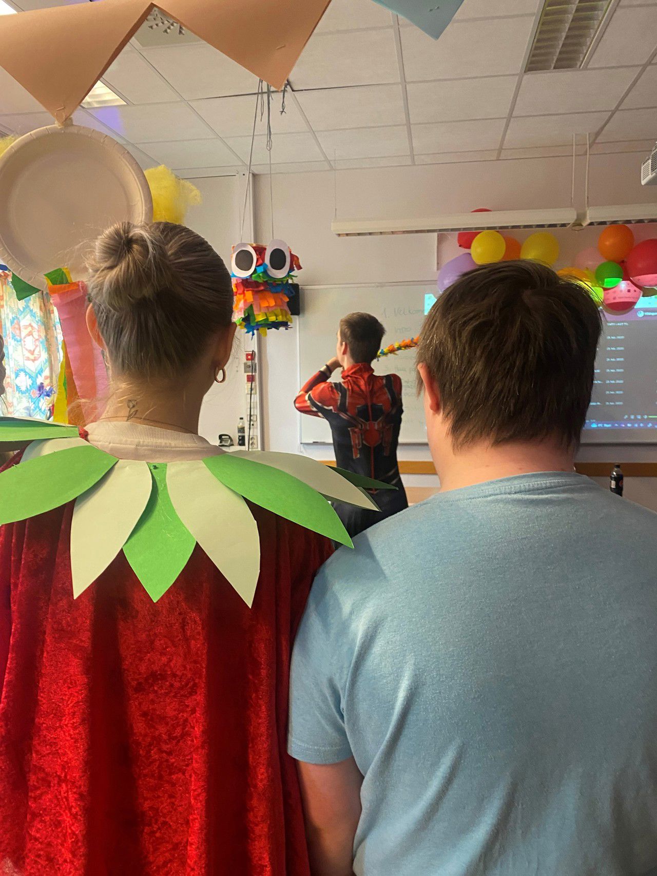 Gut i Spider Man-kostyme slår på pinjata. Elev frå 2BUa og elev frå HTH ser på.