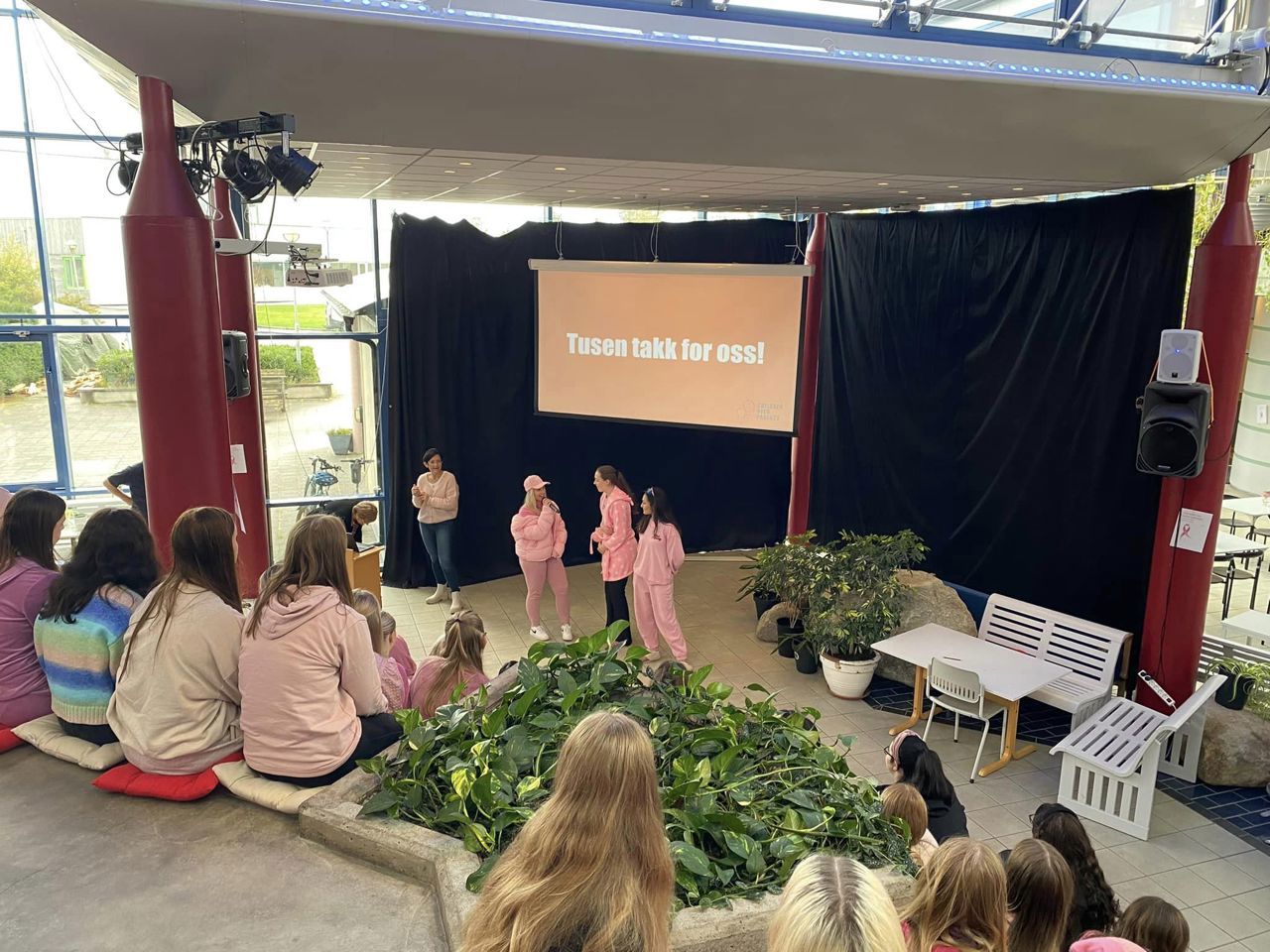 Tre elevar i rosa snakkar i mikrofon. På skjermen står det "Takk for oss"