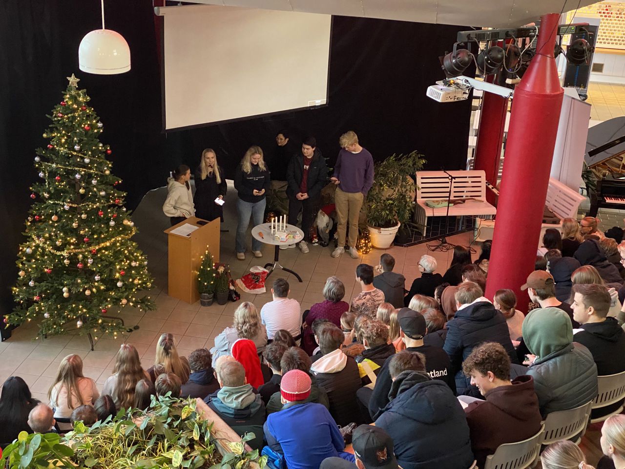 Mange elevar står fram ved juletreet. Dei snakkar i mikrofon.